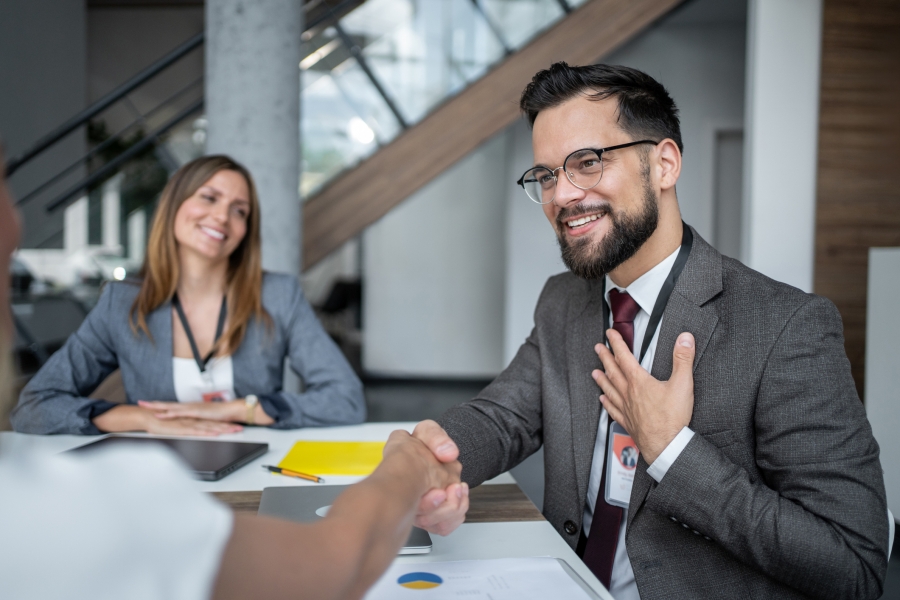 A man and woman engaged in a handshake at a meeting, indicating a positive interaction in the IT hiring process.