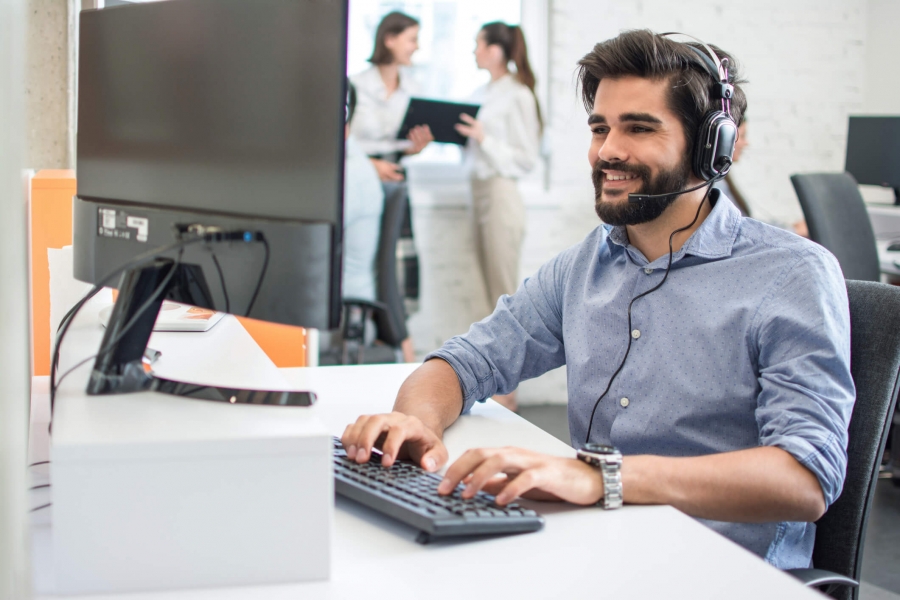 A man wearing headphones and a headset is intently working on a computer, indicating a professional environment.