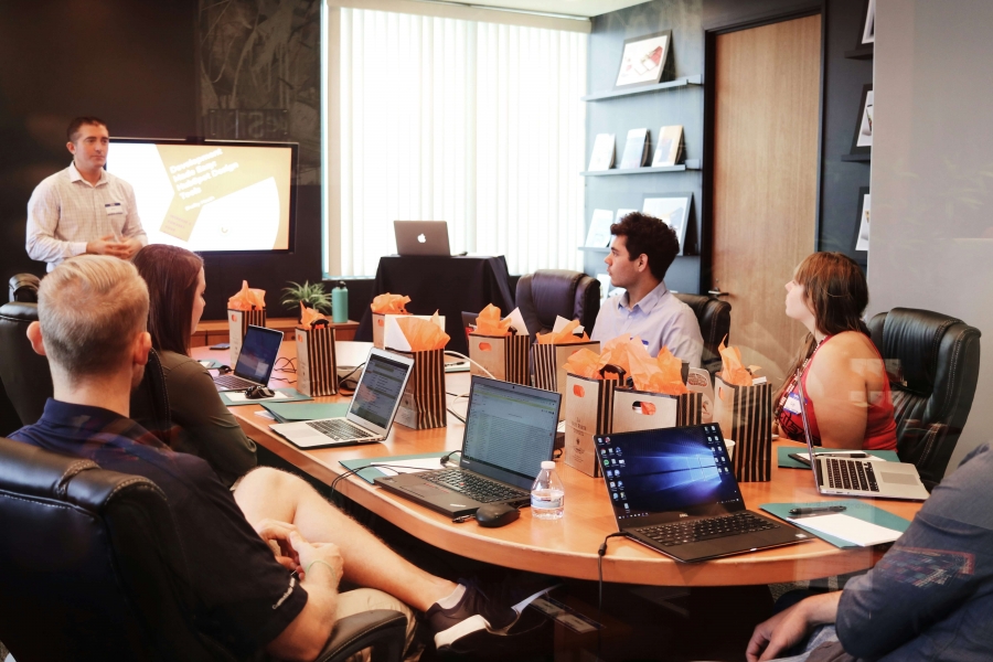 A group of people engaged in a meeting, sitting around a table with laptops open in front of them.