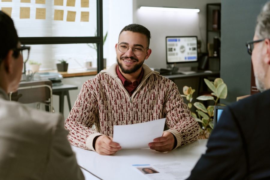 Three men at a table; one man smiles during an IT interview, while the other two listen attentively.
