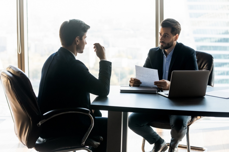 Two men engaged in discussion at a table in a modern office setting.