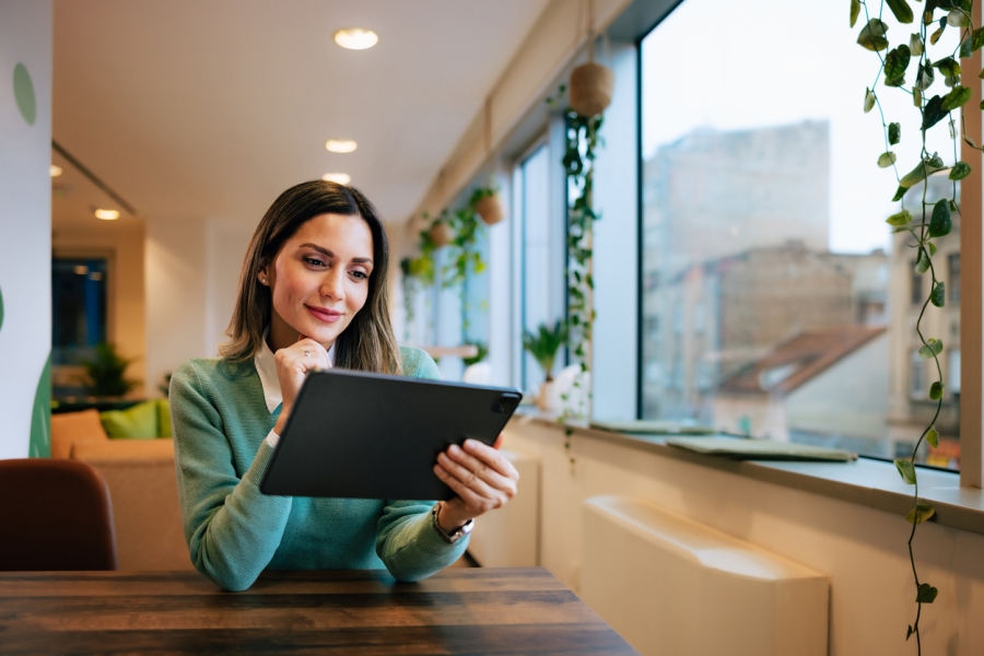A woman seated at a table, focused on her tablet computer, with a thoughtful expression on her face.